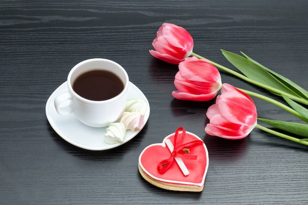 Tazza di caffè, biscotto di pan di zenzero a forma di cuore e tulipani rosa