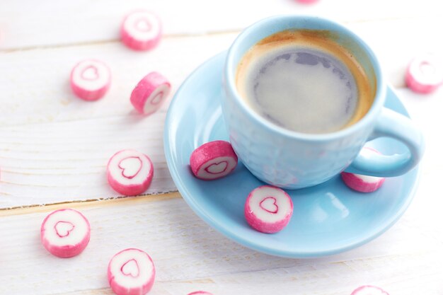 Tazza di caffè blu con cuori di caramelle, in piedi sul tavolo di legno bianco. Dolce San Valentino