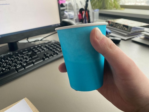 Tazza di caffè blu di cartone da una caffetteria su un desktop con un computer con una tastiera