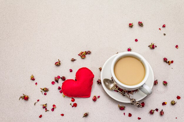Tazza di caffè, boccioli di rosa e petali e cuore di feltro rosso