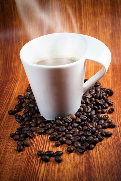 Tazza di caffè calda e fagioli con fumo.