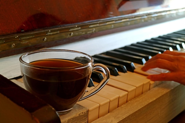 Tazza di caffè caldo al pianoforte con la mano sfocata del pianista sullo sfondo