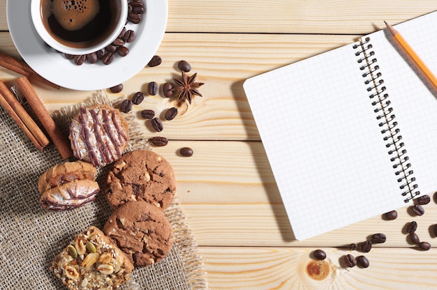 Tazza di caffè caldo, biscotti e blocco note su un tavolo di legno, vista dall'alto