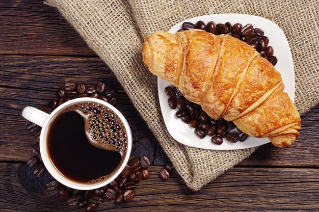 Tazza di caffè caldo con croissant per colazione su un tavolo di legno rustico, vista dall'alto