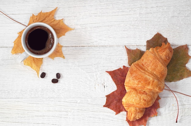 Tazza di caffè caldo con croissant su fondo di legno bianco, vista dall'alto