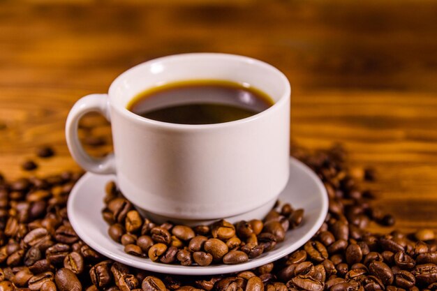 Tazza di caffè caldo e chicchi di caffè sparsi sulla tavola di legno rustica