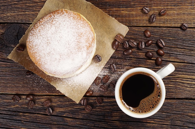 Tazza di caffè caldo e ciambella con zucchero a velo sul tavolo di legno scuro. Vista dall'alto