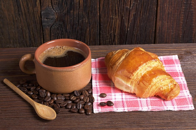 Tazza di caffè caldo e croissant fresco sul tavolo di legno scuro