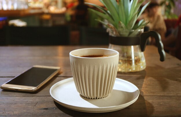 Tazza di caffè caldo su un tavolo di legno con Smartphone sfocato e pianta in vaso