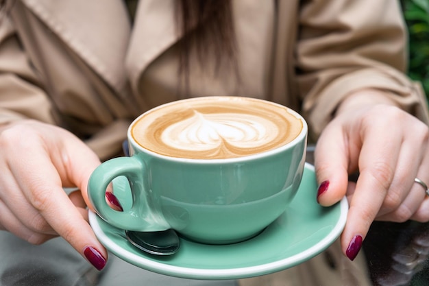 Tazza di caffè cappuccino o latte nelle mani della donna all'aperto in caffetteria o bar Classico latte art a forma di cuore