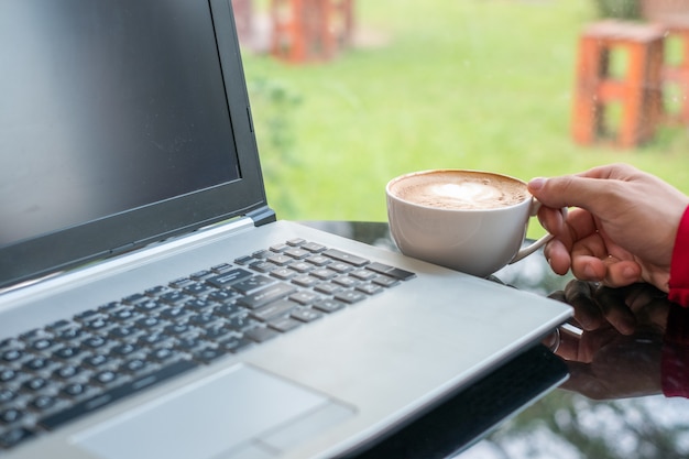 Tazza di caffè casuale della tenuta dell&#39;uomo con il computer portatile in ufficio