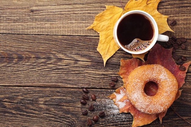 Tazza di caffè, ciambella e foglie di autunno su uno sfondo di legno