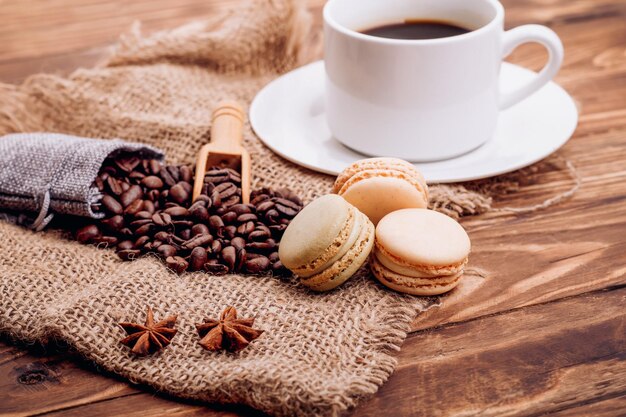 Tazza di caffè con bastoncini di cannella amaretti all'anice e chicchi di caffè su fondo di legno