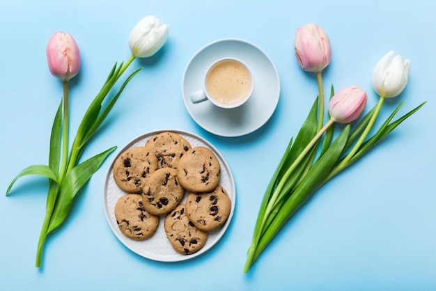 Tazza di caffè con biscotti al caffè e tulipani su uno sfondo colorato Vista dall'alto del biglietto di auguri primaverile