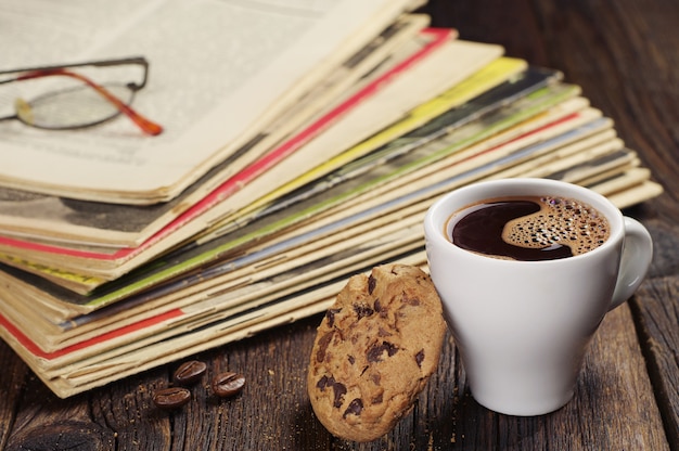 Tazza di caffè con biscotto e vecchie riviste sul tavolo di legno