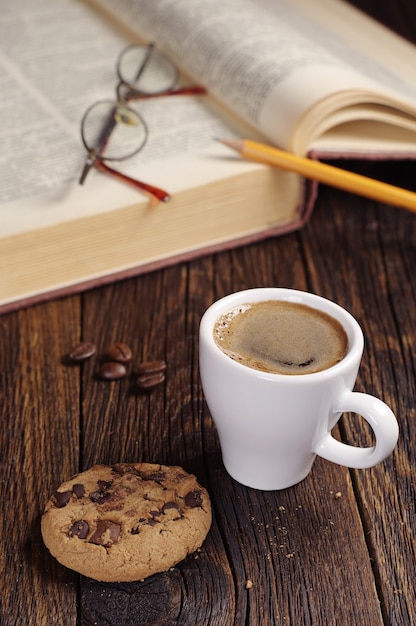 Tazza di caffè con biscotto e vecchio libro sulla tavola di legno scuro