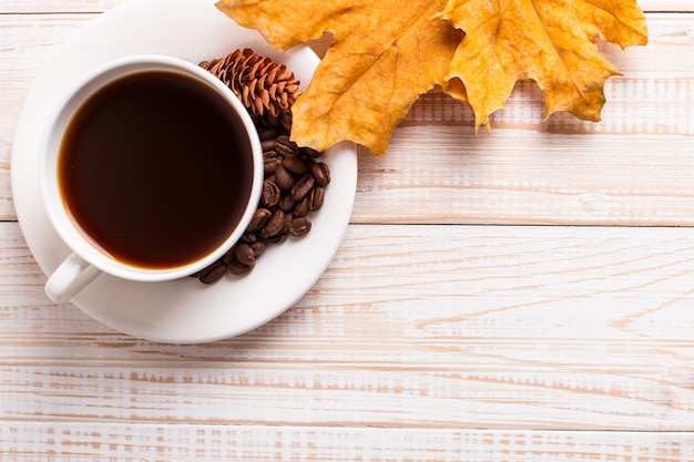 Tazza di caffè con chicchi di caffè sparsi, foglie gialle secche su un tavolo di legno. Umore di mattina d'autunno, copyspace.