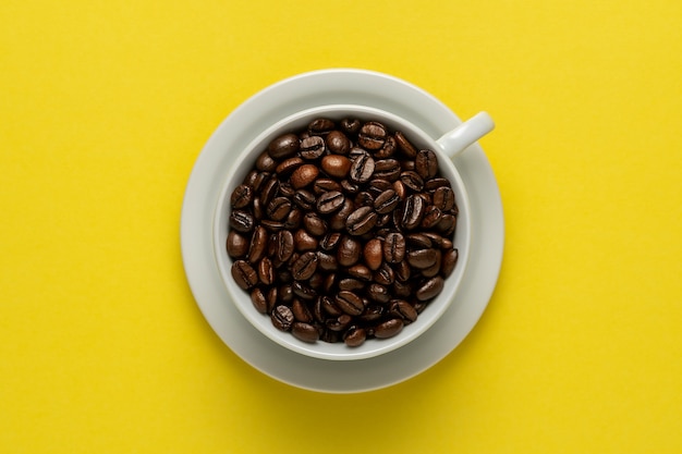 Tazza di caffè con chicchi di caffè sulla superficie gialla.