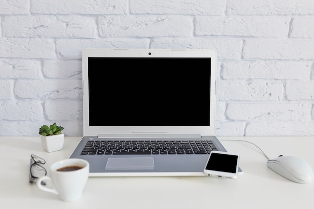 Tazza di caffè con computer portatile e telefono cellulare sullo scrittorio bianco