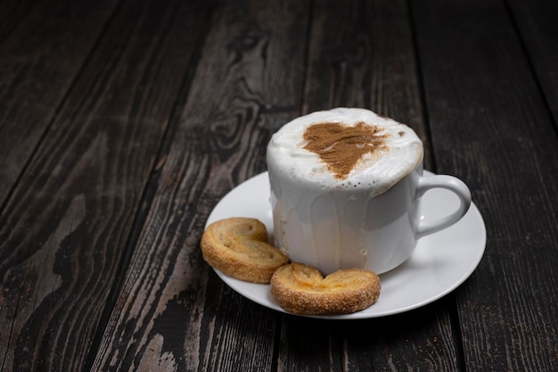 Tazza di caffè con crema e cuore di cacao per San Valentino su uno sfondo di legno scuro