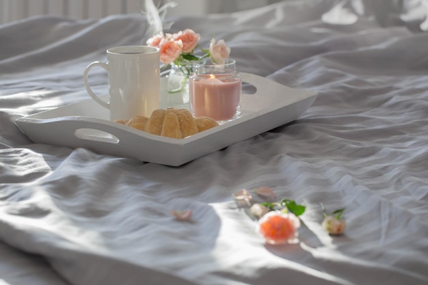 Tazza di caffè con croissant e rose rosa sul letto in camera da letto