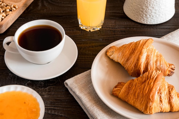 Tazza di caffè con croissant su un tavolo rustico in legno scuro Serie di alimenti Due gustosi cornetti freschi marmellata succo d'arancia Colazione continentale servita con pasticceria appena sfornata Vista ravvicinata Buongiorno