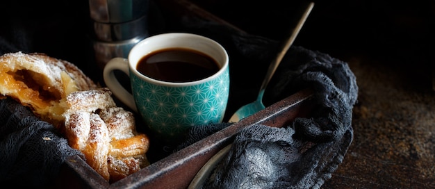 Tazza di caffè con croissant su uno sfondo scuro da vicino