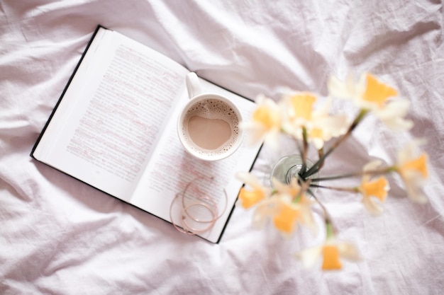 Tazza di caffè con fiori che restano sul libro aperto a letto Buongiorno Vista dall'alto