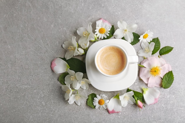 Tazza di caffè con fiori freschi in giro sul colore di sfondo