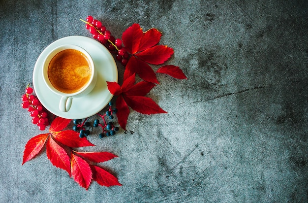 Tazza di caffè con foglie autunnali rosse e bacche su uno sfondo di cemento