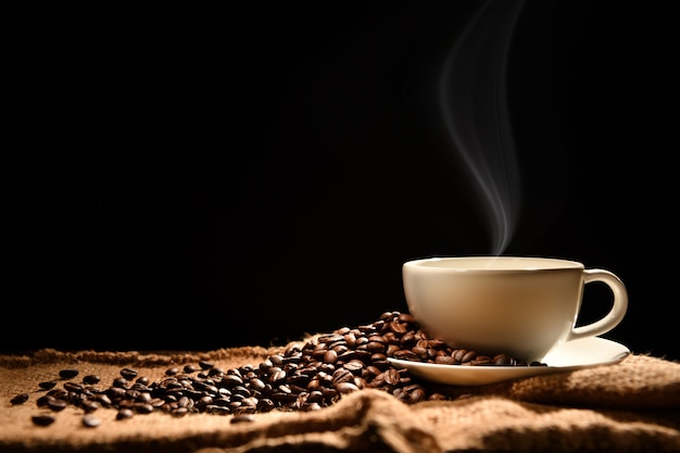 Tazza di caffè con fumo e chicchi di caffè su fondo di legno