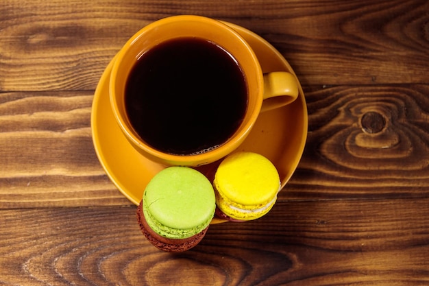 Tazza di caffè con gustosi macarons colorati sulla tavola di legno. Vista dall'alto