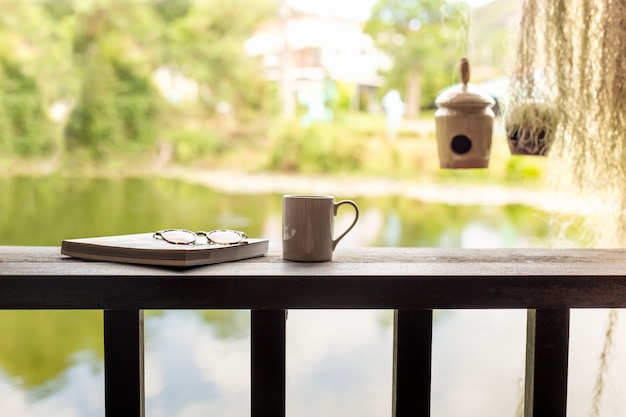 Tazza di caffè con i vetri dell'occhio e del libro sulla cima di legno.