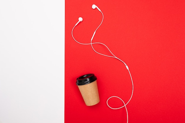 Tazza di caffè con le cuffie bianche sulla parete rossa e bianca