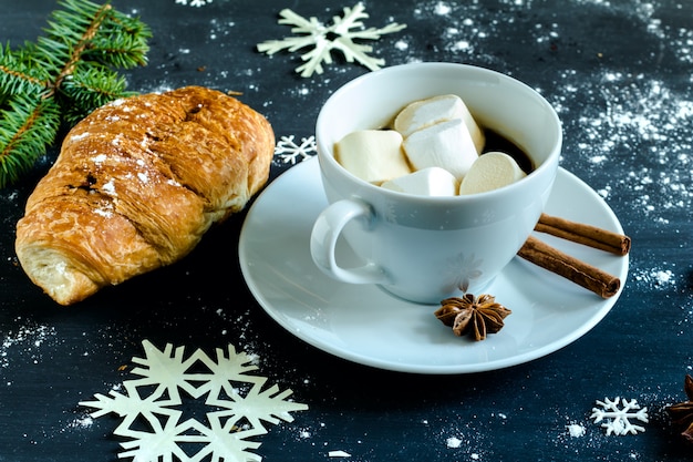 Tazza di caffè con marshmallow, cornetto, cannella e anice stellato.