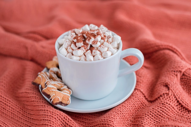 Tazza di caffè con marshmallow e biscotti di stelle sulla coperta di corallo a maglia calda.