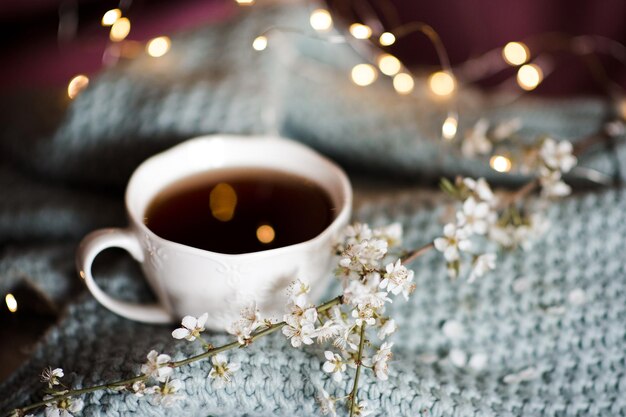 Tazza di caffè con ramo fiorito di fiori sul primo piano di stoffa a maglia. Stagione primaverile. Buon giorno.