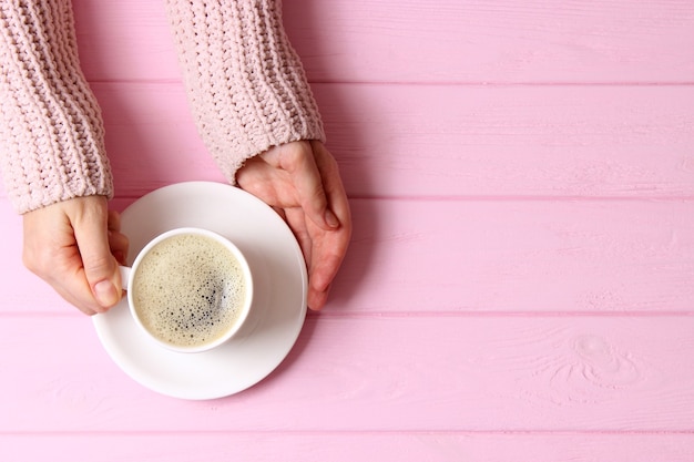 Tazza di caffè con schiumoso in mani femminili sulla vista del piano del tavolo in legno