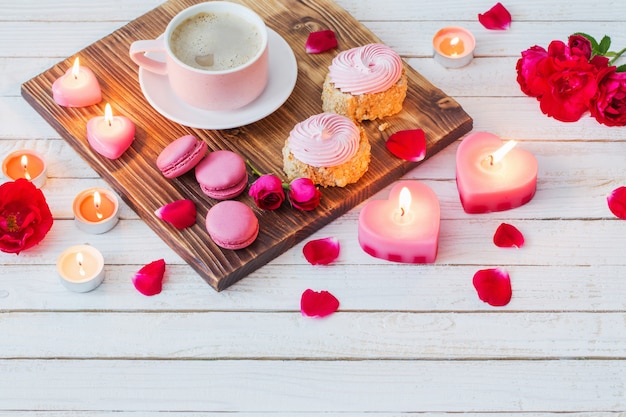 Tazza di caffè con torte, candele e rose sul retro in legno bianco