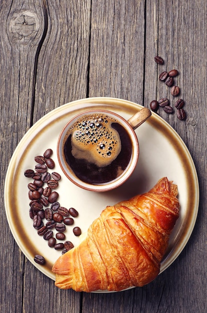 Tazza di caffè con un croissant su un piatto su un tavolo di legno. Vista dall'alto