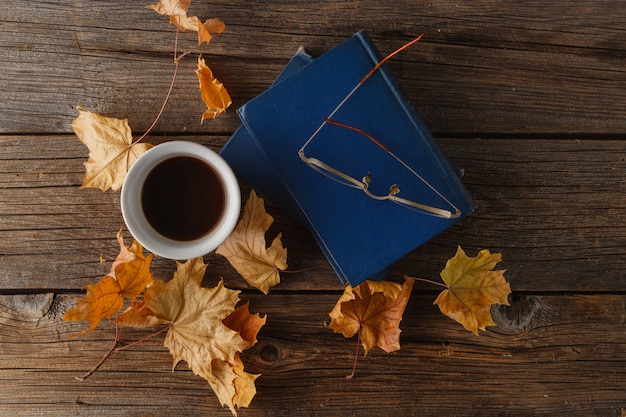 Tazza di caffè con un vecchio libro e foglie di quercia. Su fondo in legno.