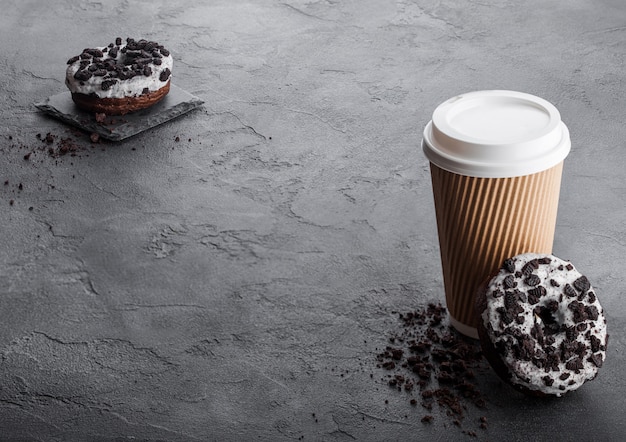 Tazza di caffè del cartone con le ciambelle nere dei biscotti sul tavolo da cucina di pietra nero. Bevanda e snack al caffè.