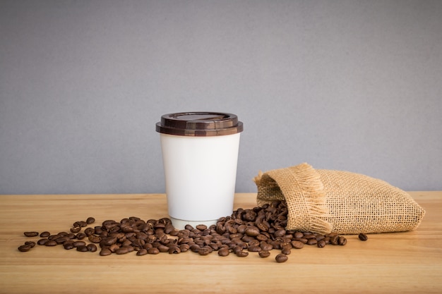 Tazza di caffè del Libro Bianco con i chicchi di caffè sullo scrittorio di legno