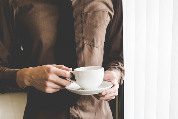 Tazza di caffè della tenuta dell'uomo d'affari alla finestra. Idea di avvio di business creativo.