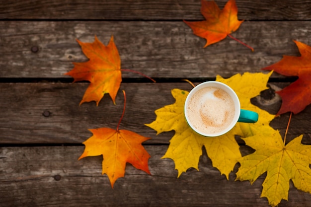 Tazza di caffè di cappuccino e foglie di autunno su vecchie tavole di legno scure di superficie.