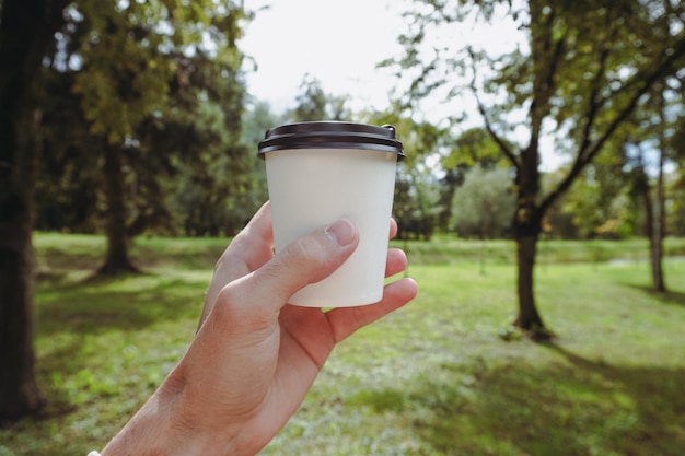 Tazza di caffè di carta della tenuta della mano. Tazza di carta bianca per caffè su uno sfondo di erba.