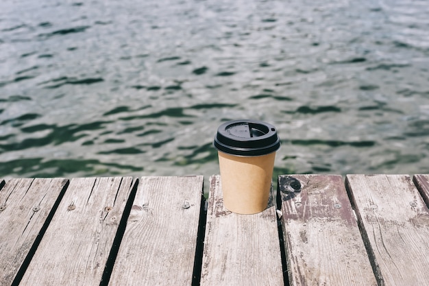 Tazza di caffè di carta sul mare vicino di legno