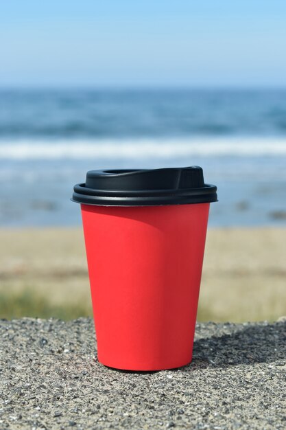 Tazza di caffè di carta sullo sfondo del mare sulle pietre