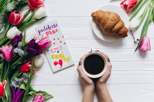 Tazza di caffè di holding femminile su una priorità bassa bianca di legno con i tulipani freschi.