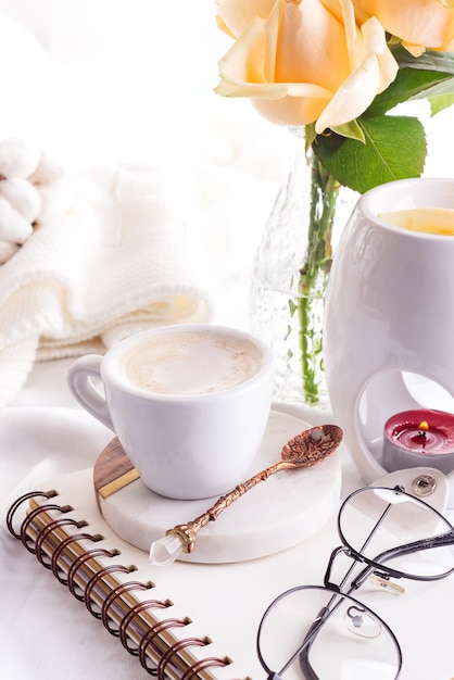 Tazza di caffè di mattina con gli occhiali su un taccuino, una candela e una rosa